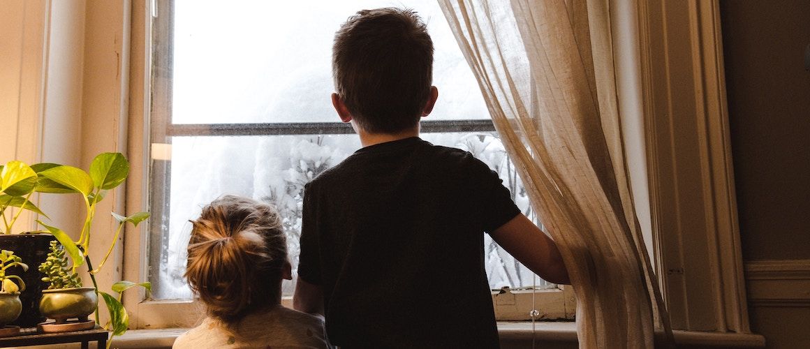 Children looking outside outdated window at snowfall.