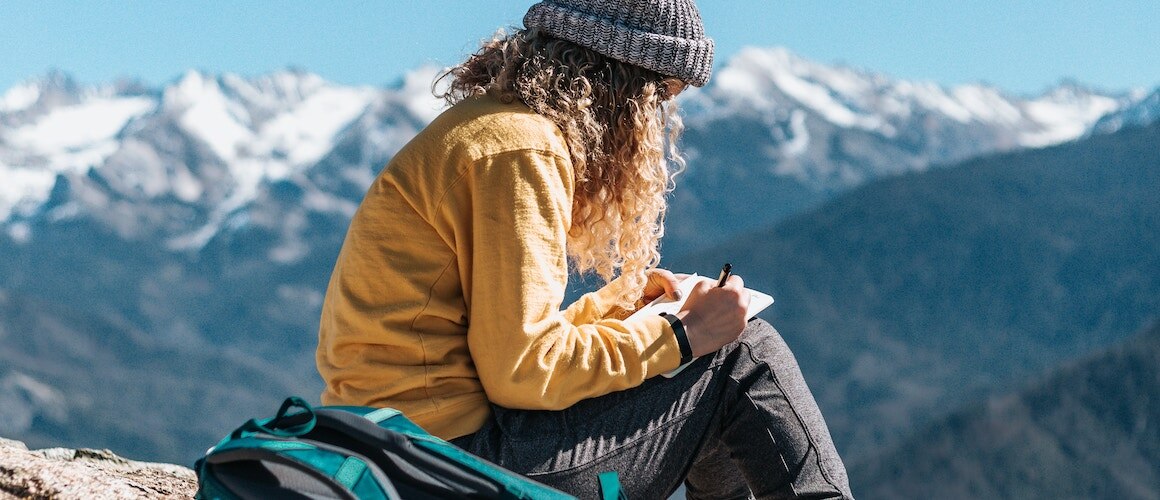 Image of girl journaling and evaluating her finances on mountain.