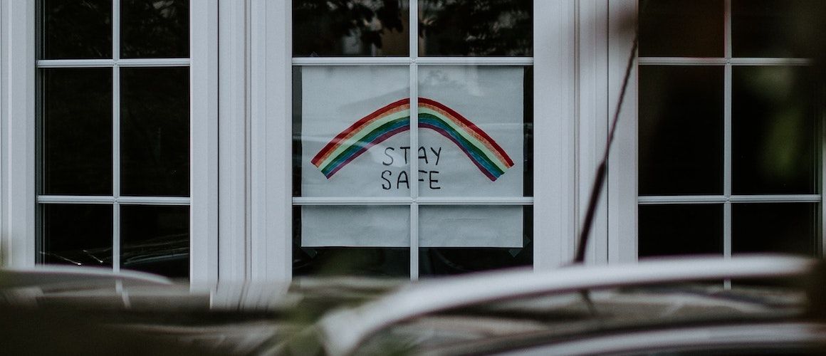 Image of colorful handmade "stay safe" sign in window.