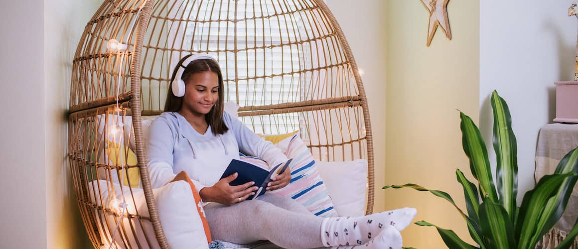 Image of daughter with headphones sitting in wicker chair reading in her room, surrounded by twinkling lights