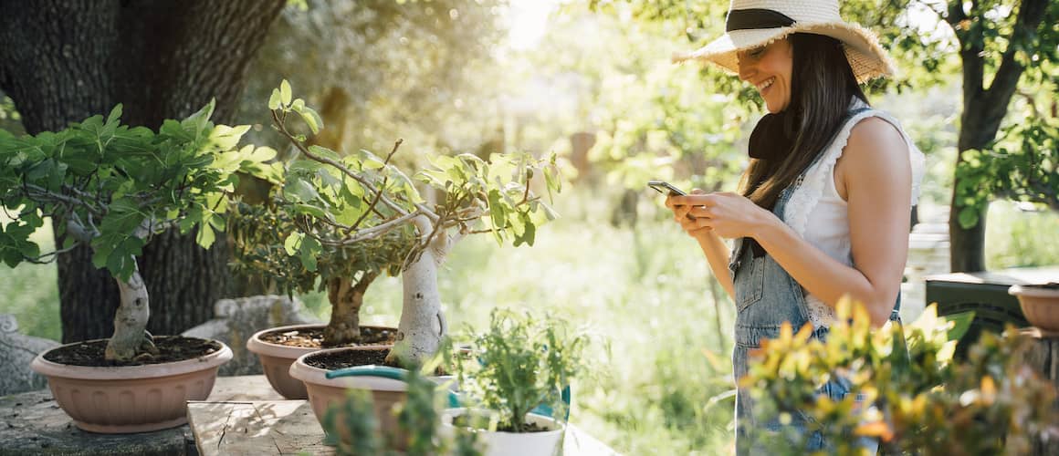 Image of woman creating green landscape in her back yard, pausing and smiling at her phone.