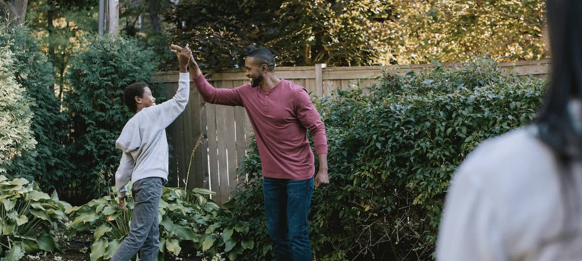 Image of smiling dad giving son a high five in the back yard.