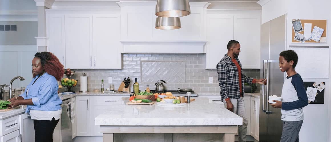Image of family in white, sustainable kitchen preparing a meal.