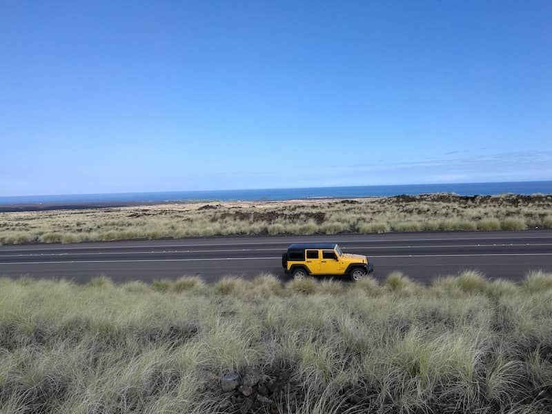 Bright yellow jeep wrangler driving down a rural road.