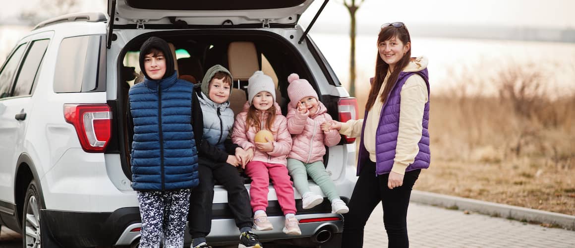 A mother and her kids bundled up and sitting in the trunk of a white SUV.