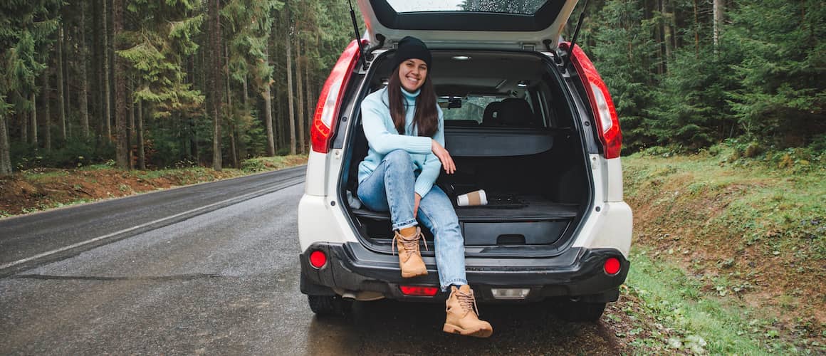 Woman sitting in SUV trunk surrounded by forest.