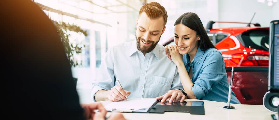 Young couple signing documents at a car dealership.
