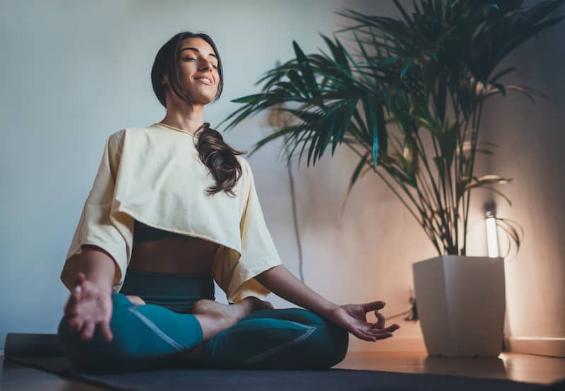 Woman doing relaxing yoga in basement next to plant.