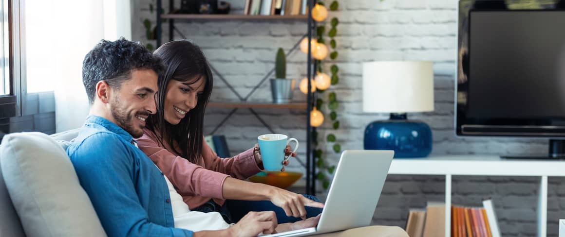 Young happy couple looking at homes on laptop in apartment.