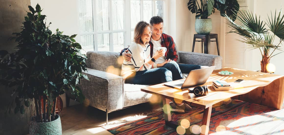 A happy couple at home on the couch watching movie using their laptop.