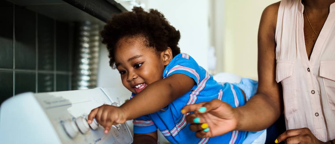 Young child on top of washing machine using the dials with their mother.