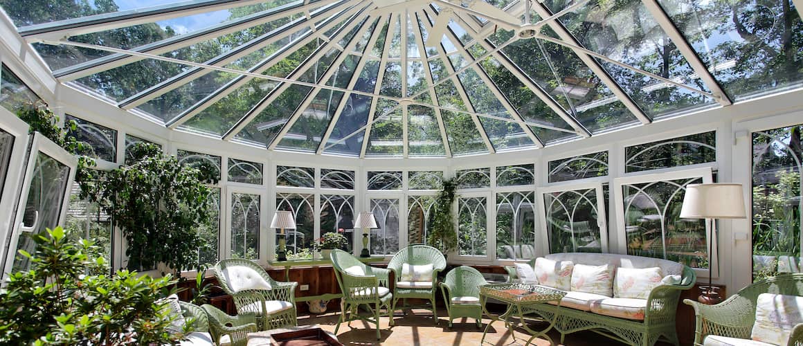 Large circular sunroom with wicker furniture and many plants.