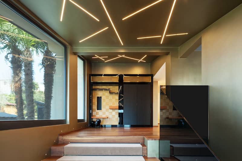 Accent art ceiling with abstract neon lights in stairwell with large picture window to the left overlooking palm tree trunks.