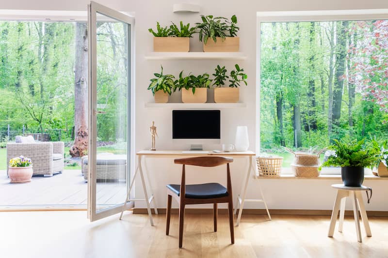 Zen style home office with large windows overlooking lush green landscape.