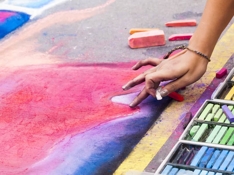 Close up view of someone's hand drawing a chalk image onto the ground.