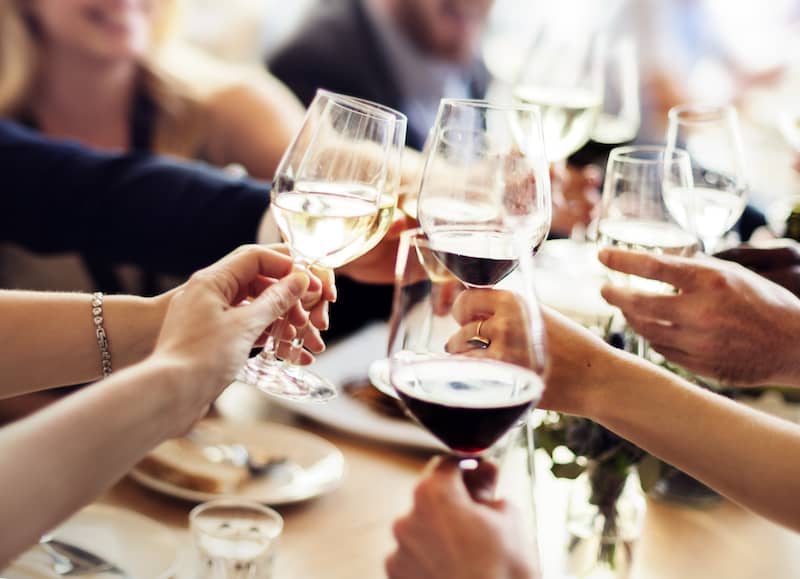 Close up view of people celebrating by clinking their wine glasses together at a restaurant.