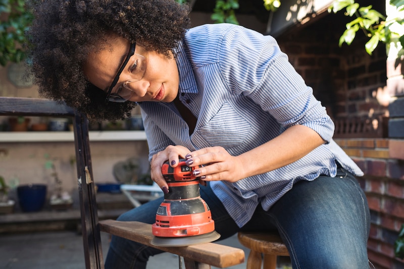 Woman sanding wood plank with safety glasses.