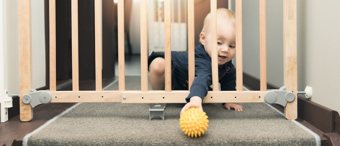 Toddler reaching through baby gate to get a ball