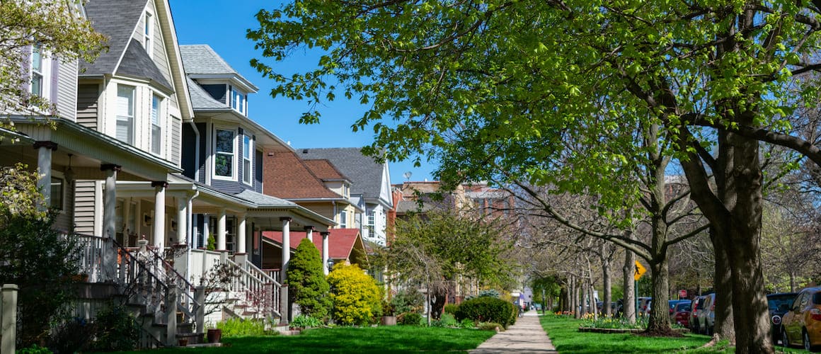 Row of older wood homes with porches on a tree lined neighborhood street.