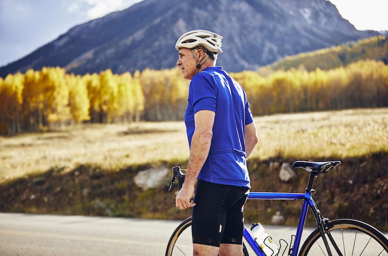 Older man standing by a mountain bike with a mountain behind him