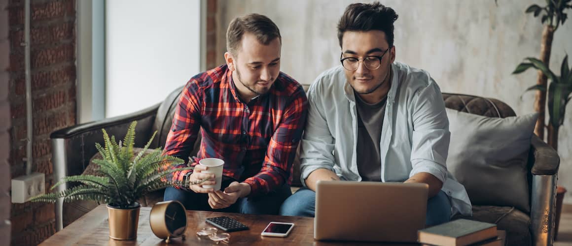 Same-sex couple sitting on couch looking at laptop on coffee table.