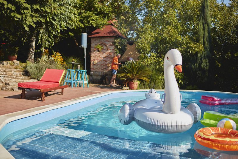 swan pool float surrounded by other floaties in in-ground pool