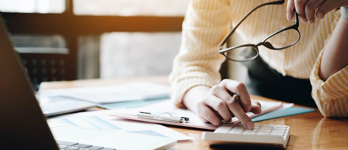person holding glasses balancing checkbook with calculator