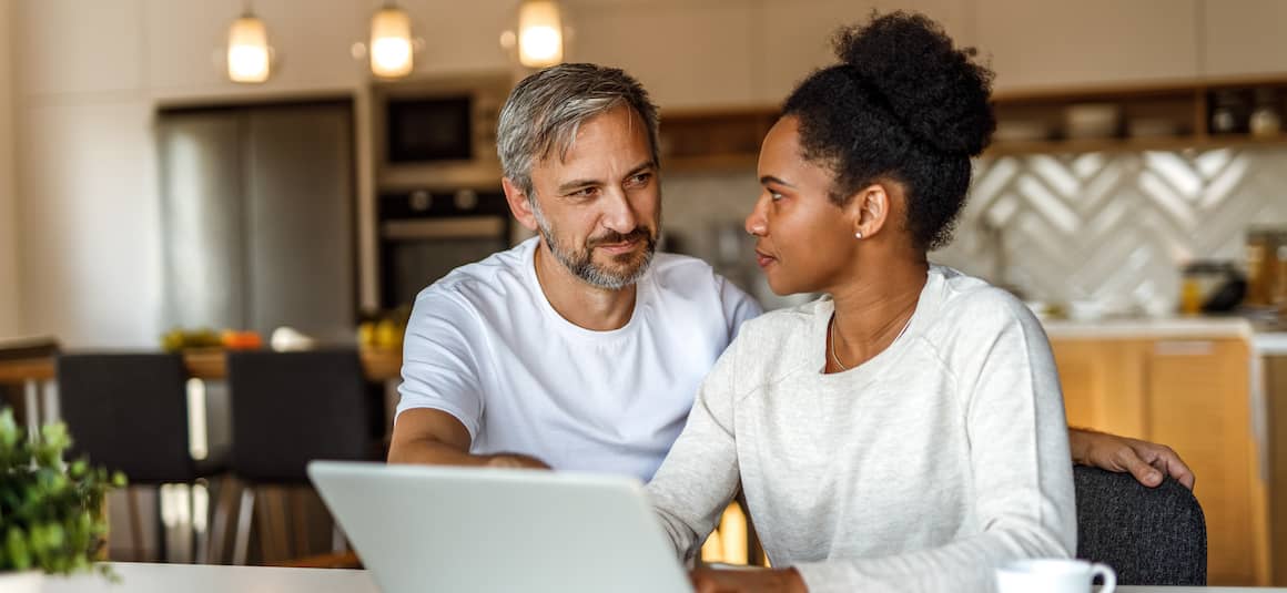 Couple sitting at breakfast table looking on laptop together.