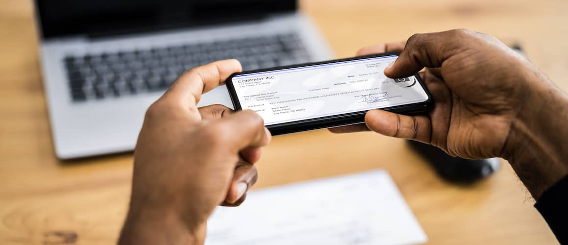 man taking picture of check with laptop in background