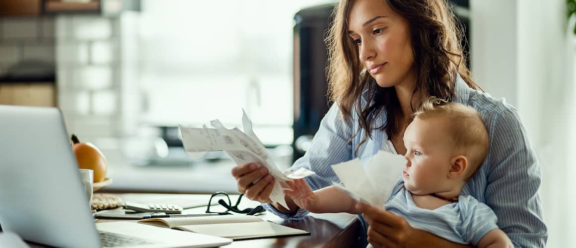 Woman with young child on lap calculating finances on laptop.