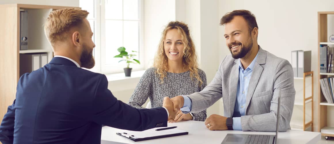 Young happy couple shaking hands with a real estate agent.