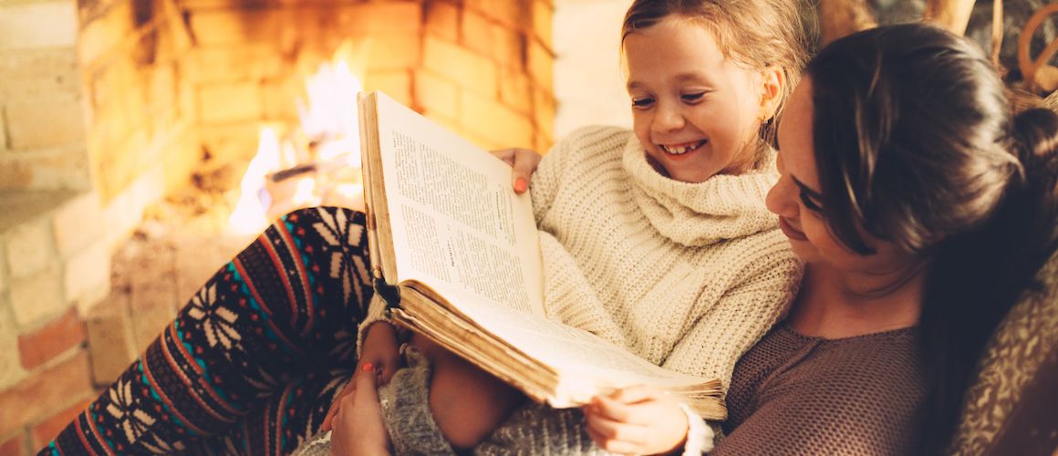 Mother and daughter reading by the fire at holiday time.