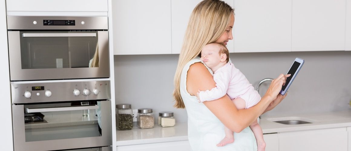 Mom and baby standing in a kitchen, mom is checking her Credit Score.