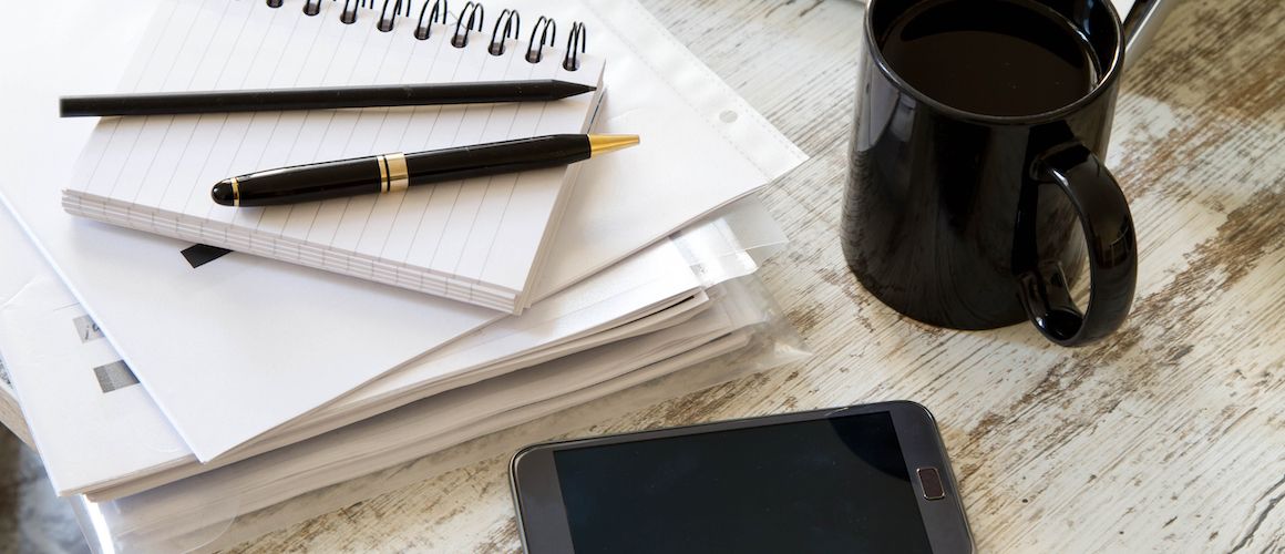 Paper notebooks, smart phone and laptop on desk.