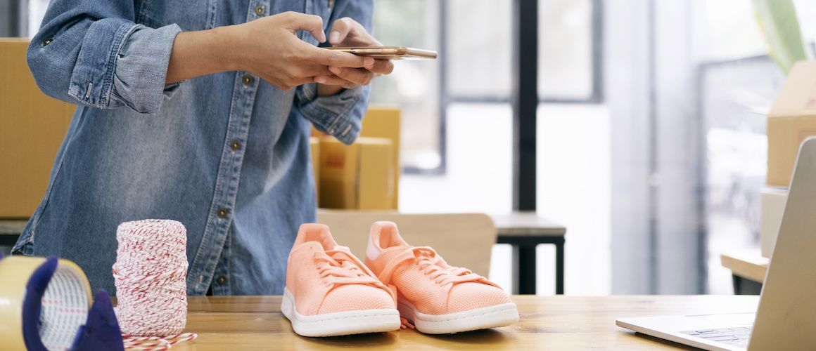 woman taking a picture on her phone of a pair of pink tennis shoes