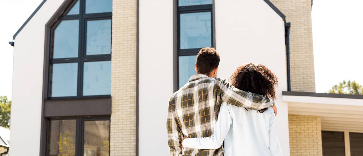 couple embracing while viewing front of house in neighborhood