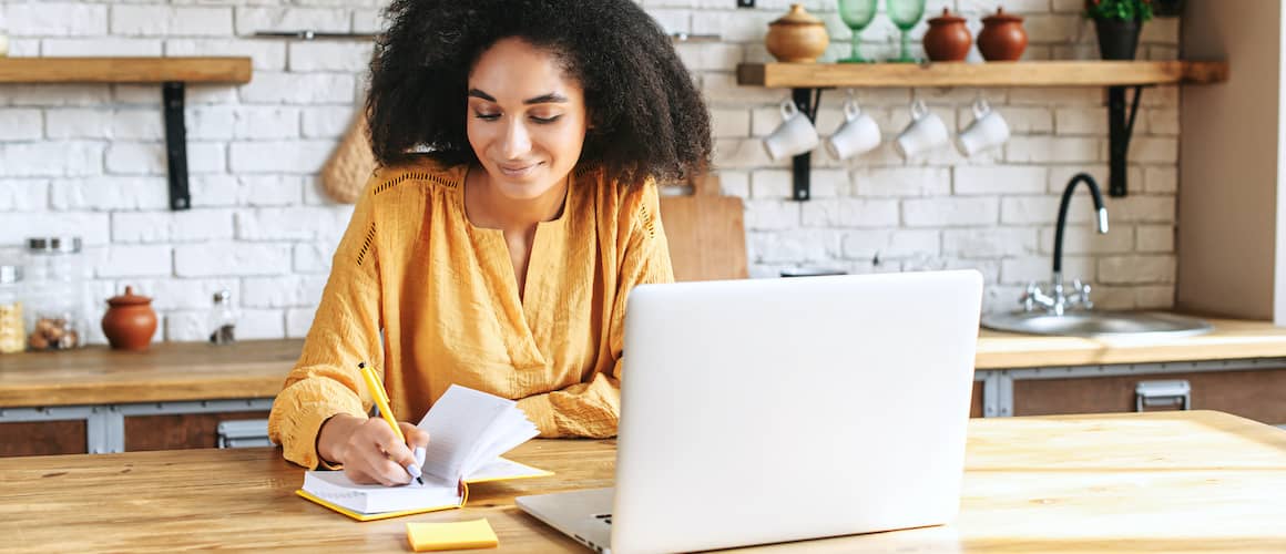 woman writing and on laptop in kitchen