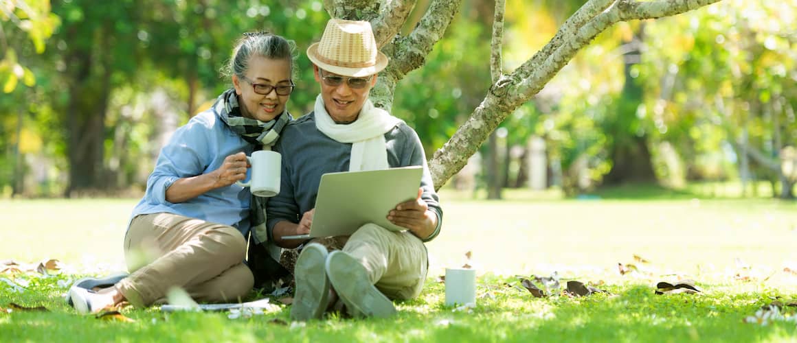 Retired couple having coffee together under a tree outside.